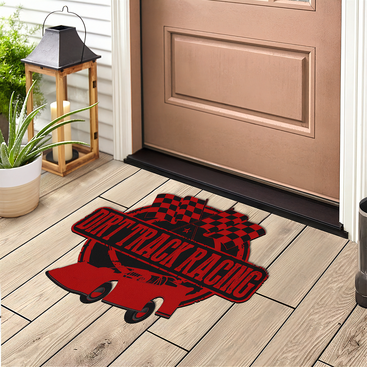 A red and black 'Drift Track Racing' doormat featuring a race car and checkered flag design, shown on a light wood porch floor in front of a tan front door.