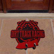 A red and black 'Dirt Track Racing' doormat featuring a race car, checkered flags, and a circular emblem, displayed on a tan stone floor in front of a dark wood door.