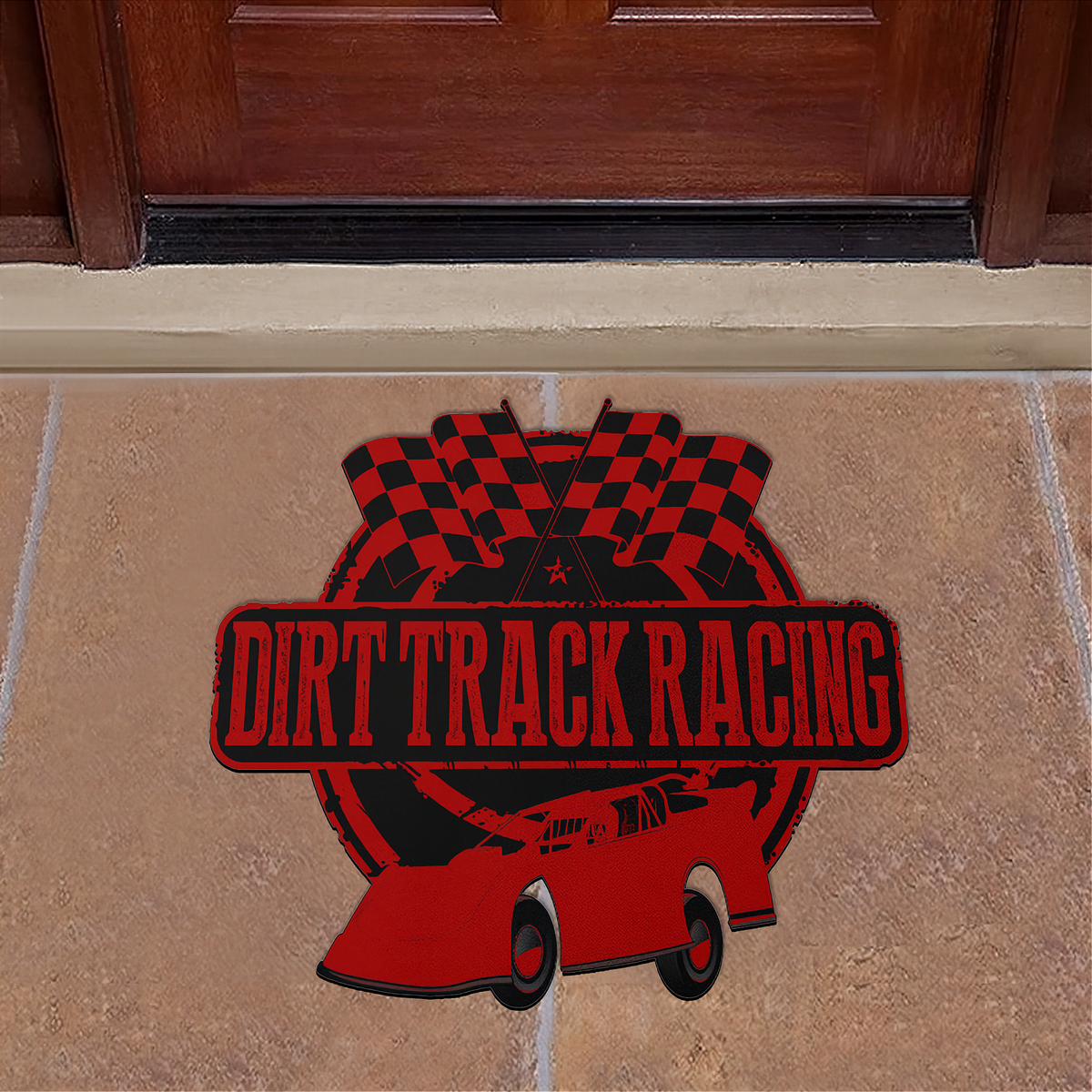 A red and black 'Dirt Track Racing' doormat featuring a race car, checkered flags, and a circular emblem, displayed on a tan stone floor in front of a dark wood door.