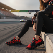 Person wearing red and black checkered shoes on a race track with a car in the background.