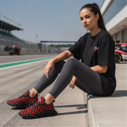 Woman sitting on a race track wearing black checkered sneakers, black t-shirt, and gray leggings.