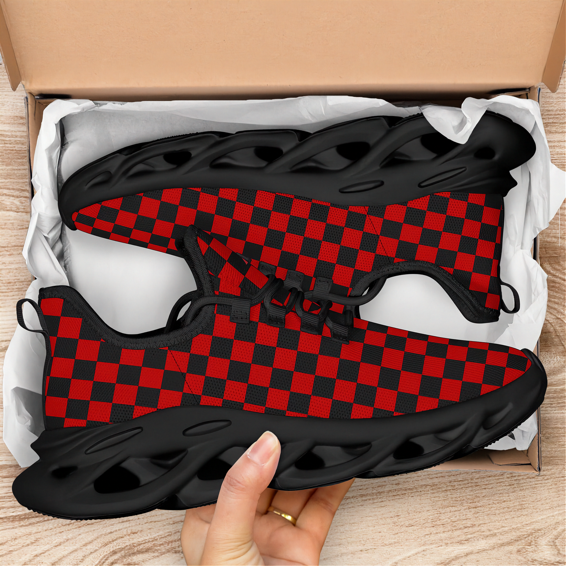 Red and black checkered sneaker with a hand holding it above an open cardboard box.