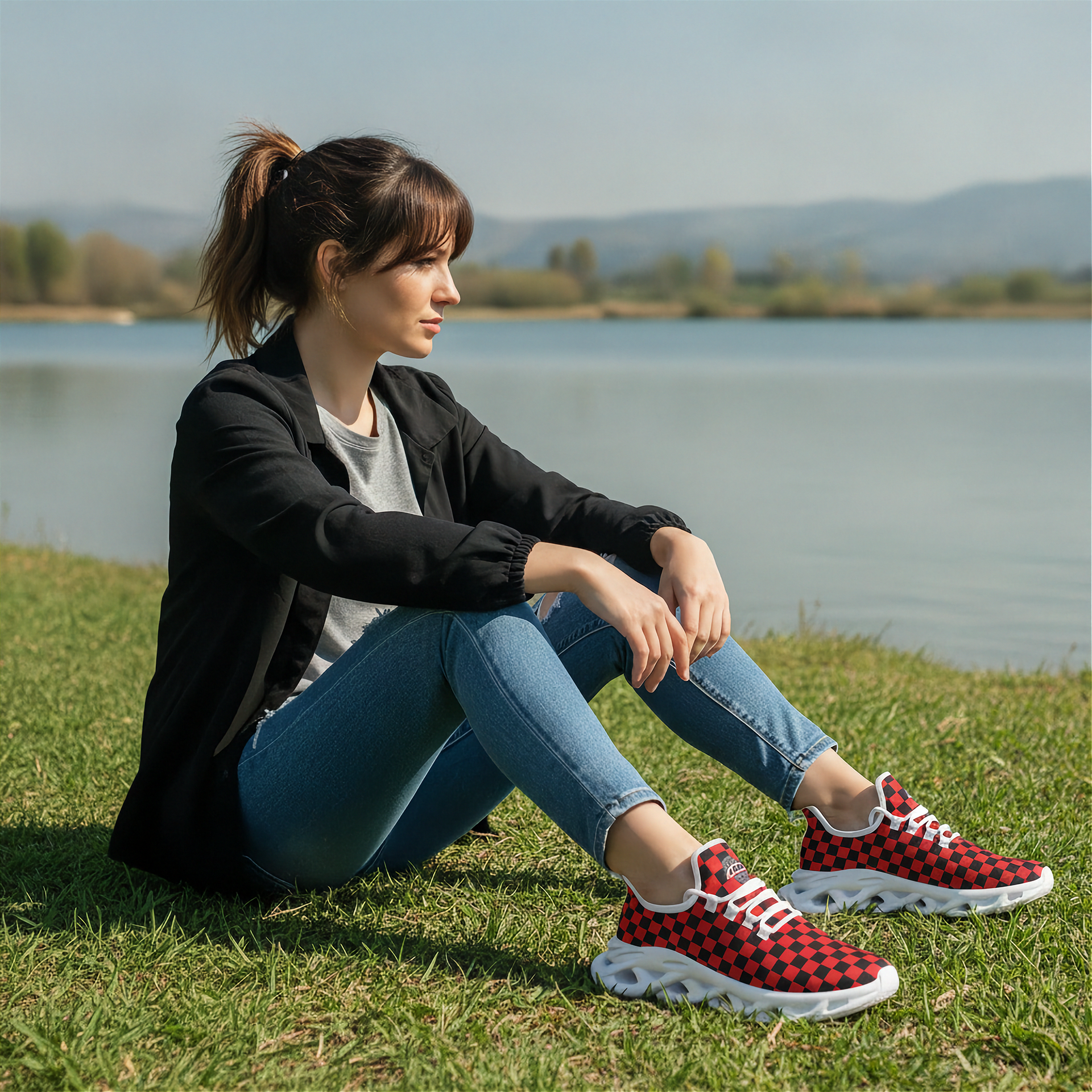 Woman sitting on grass by a lake wearing red and black checkered sneakers.