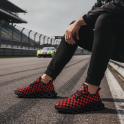 Man wearing red and black checkered shoes on a race track with a colorful car in the background.
