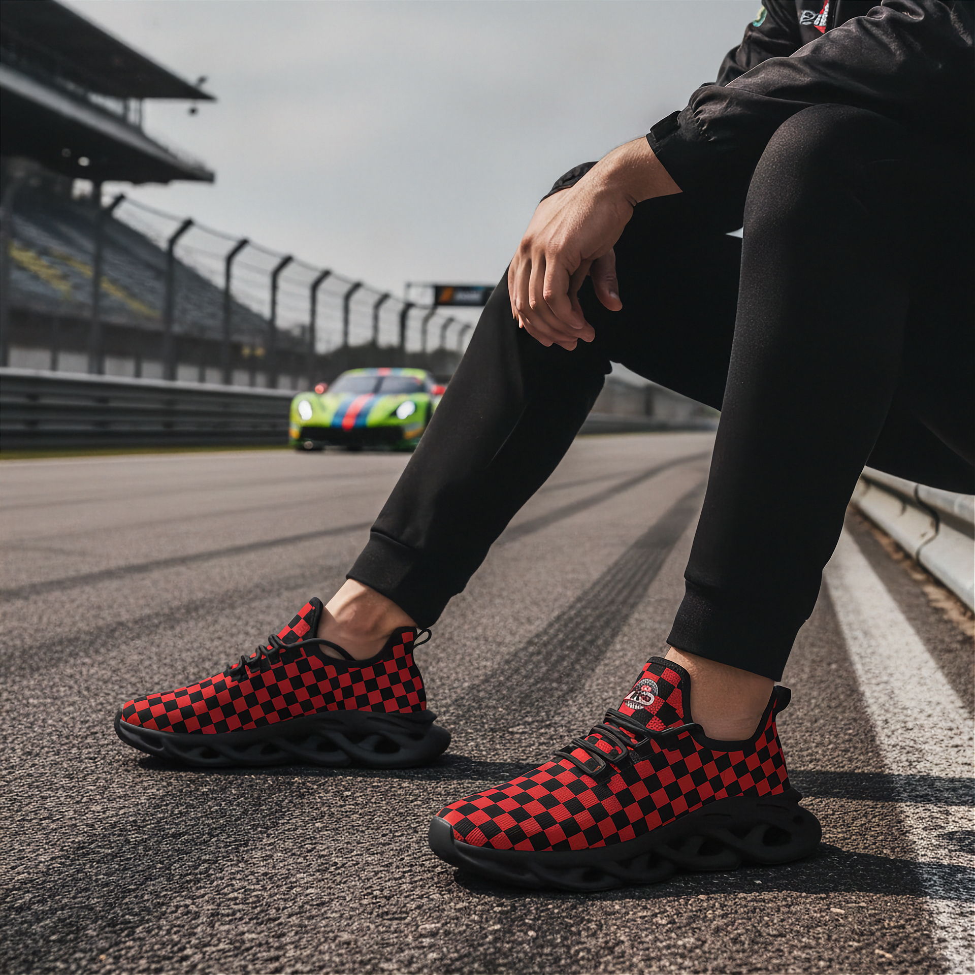 Man wearing red and black checkered shoes on a race track with a colorful car in the background.