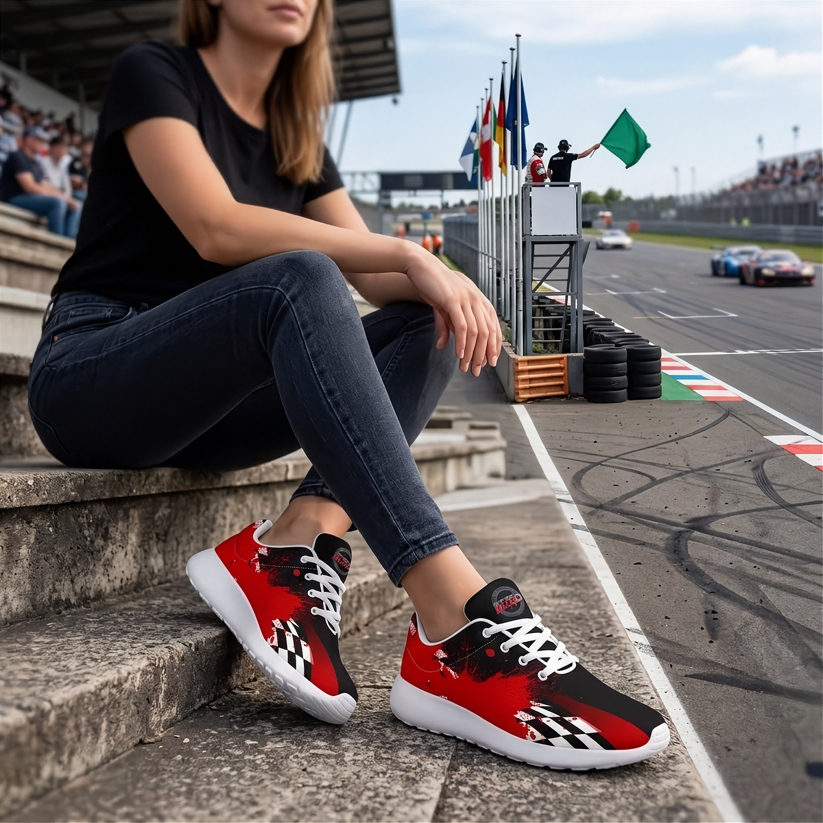 A woman sitting on concrete trackside steps at a racetrack, wearing red, black, and white checkered athletic sneakers with white laces and white soles. The racetrack, flags, and grandstands are visible in the background.