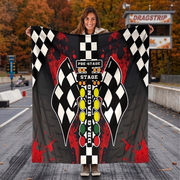 A woman stands on a racetrack holding up a large printed blanket or poster featuring a drag racing design with black-and-white checkered flags, red paint splatter, and a traffic light graphic.