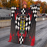 A woman stands on a racetrack holding up a large printed blanket or throw. The blanket features a black and white checkered racing design with red paint-splatter accents and a central vertical graphic reading 'PRE-STAGE STAGE CHASING RACING'.