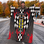 A man standing on a racetrack holds up a large black and gray racing-themed blanket or throw featuring checkered flags, red paint splatter, and a vertical 'Pre-Stage Stage Racing' graphic.