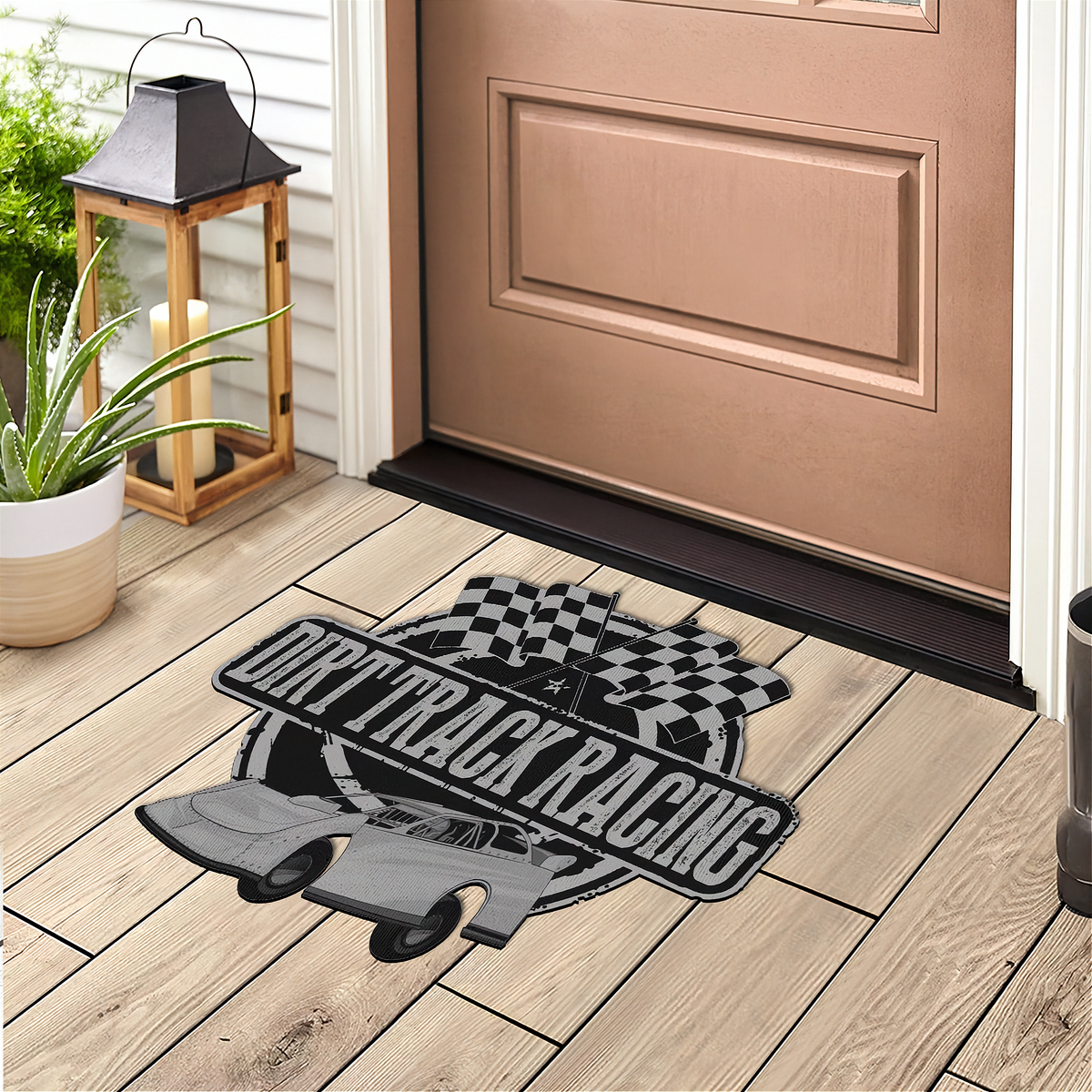 A rectangular doormat with a drift track racing design, placed on a light wood porch floor in front of a brown door. The mat features a black and gray race car, the words 'DRIFT TRACK RACING' in white, and a black-and-white checkered circle motif.