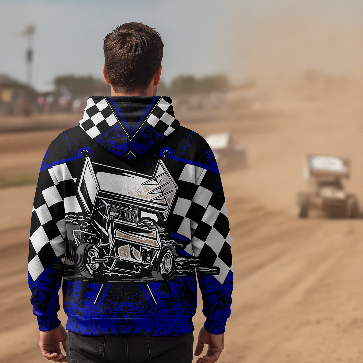 A man viewed from behind wearing a custom hooded sweatshirt with a blue and black checkered design, a large race car graphic on the back, and a blurred dirt track background.