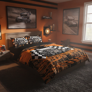A racing-themed bedding set displayed on a bed in a styled bedroom. The set features a duvet cover and matching pillowcases with a bold black and orange paint-splatter design, checkered flag patterns, and illustrations of race cars.