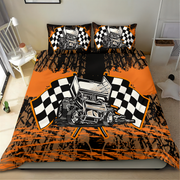 A racing-themed bedding set featuring a duvet cover and two pillowcases with a black and orange paint-splatter design, a vintage race car illustration, and checkered flags, shown on a bed in a bedroom.