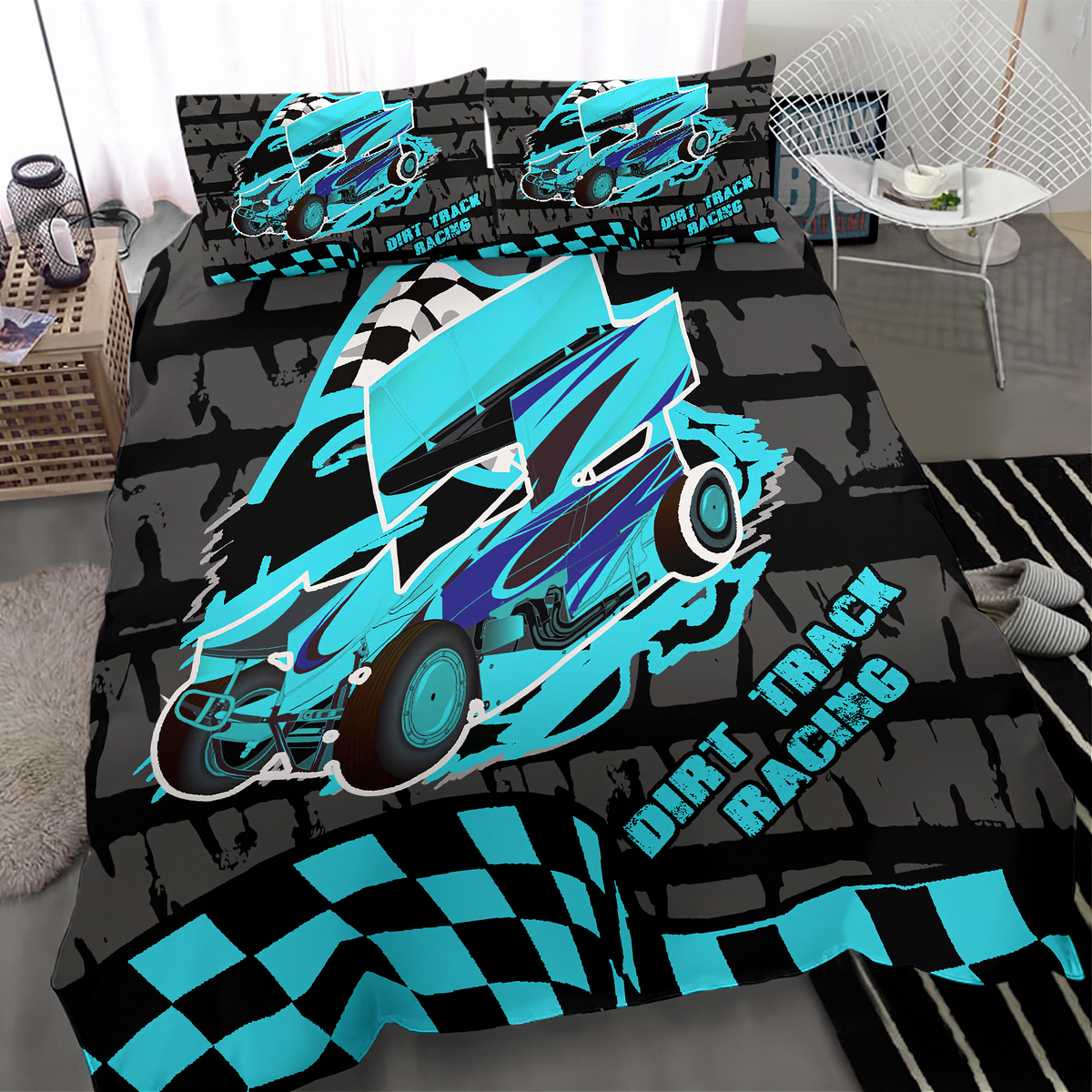 A bed dressed with a racing-themed bedding set featuring a large turquoise and black dirt track race car, checkered flag pattern, and the words 'DIRT TRACK RACING' on a dark gray background. Matching pillowcases are visible behind the bed, with a bedroom setting including a chair, rug, and side table around it.