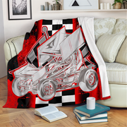 A fleece throw blanket draped over a cream sofa in a living room setting, featuring a graphic print of a silver sprint car on a red and black checkered background.