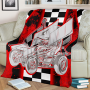 A red and black checkered blanket with a silver sprint car graphic is draped over a beige sofa in a living room setting.