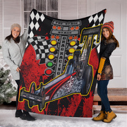 Two women holding a red-and-black dragster blanket outside a snowy home, showing the full car photo and starting-light design.