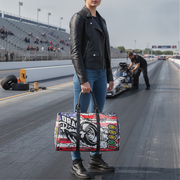 Person holding a colorful usa flag and drag racing design bag on a race track with a car and person in the background.