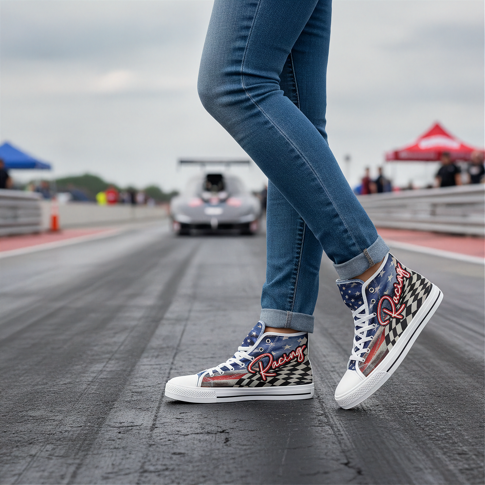 Person wearing checkered high-top sneakers on a race track with cars and tents in the background.