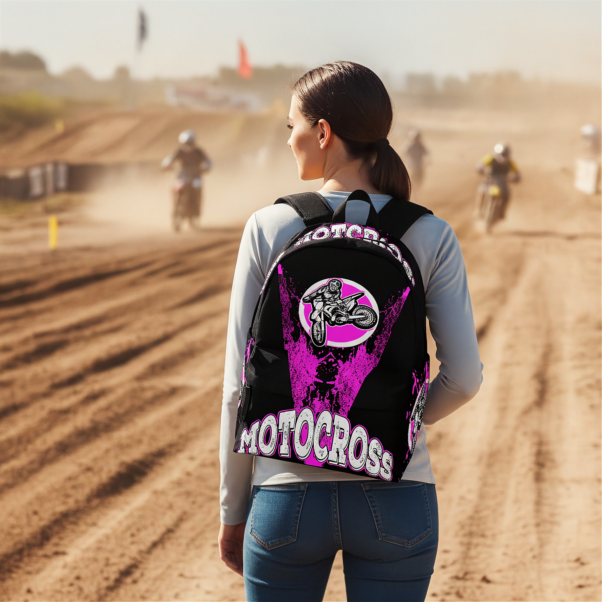 A woman on a dirt motocross track seen from behind, wearing a black backpack with a large pink and white 'MOTOCROSS' graphic on the back.