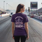 woman wearing a purple t-shirt with drag racing text at a race track.