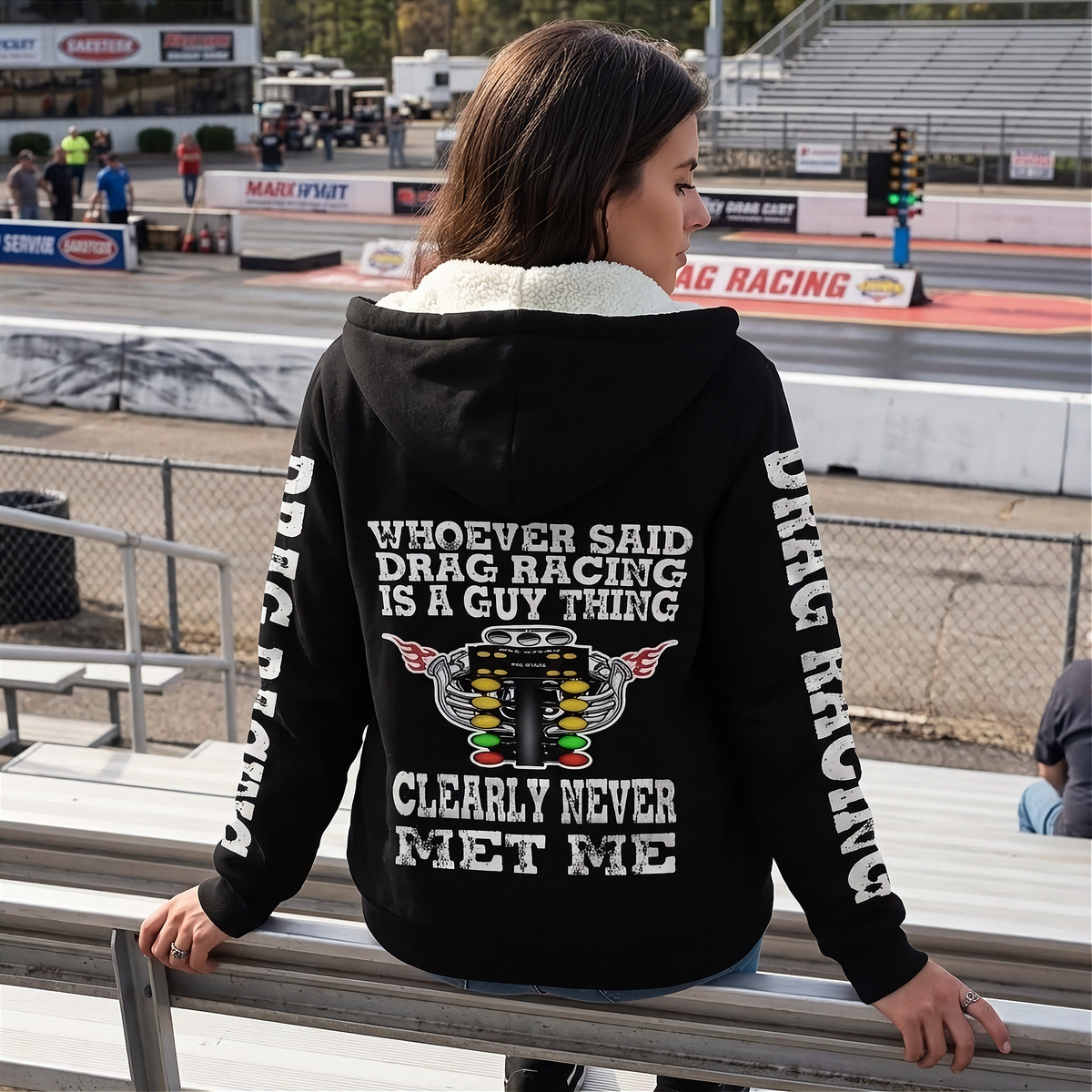 A woman modeling a black zip-up hoodie with a light beige fleece lining. The hoodie features a white graphic print on the back and white DRAG RACING on the sleeves.