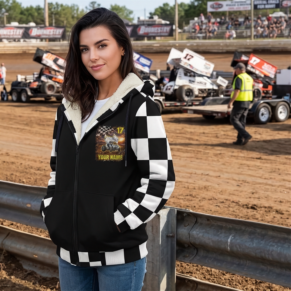 Woman wearing a personalized sprint car sherpa jacket at the track, showing the chest graphic, checkered sleeves, and white lining.