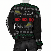 A black Christmas sweater with a festive holiday pattern, featuring snowflakes, green zig-zag stripes, reindeer, and two yellow-and-blue trucks with the text 'HO-HO-HO' in red on the back. The sweater is shown on a mannequin from the rear, paired with dark gray jeans.