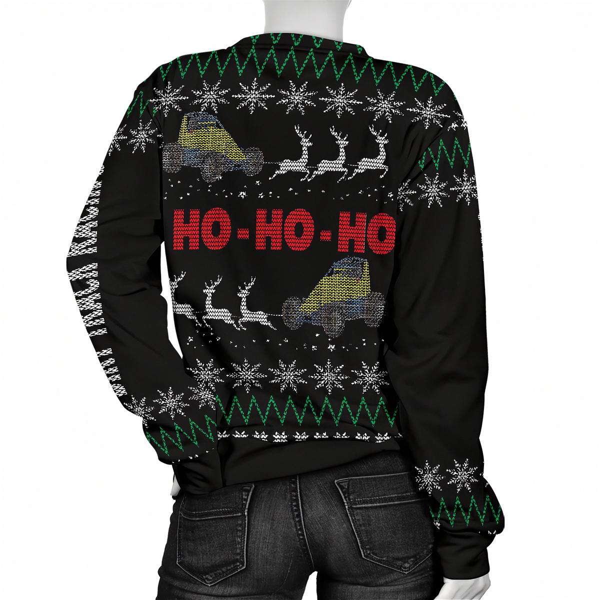 A black Christmas sweater with a festive holiday pattern, featuring snowflakes, green zig-zag stripes, reindeer, and two yellow-and-blue trucks with the text 'HO-HO-HO' in red on the back. The sweater is shown on a mannequin from the rear, paired with dark gray jeans.