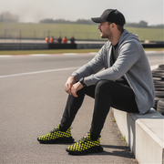 Man sitting on a race track wearing checkered shoes, gray hoodie, and black cap.