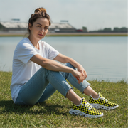 Woman sitting on grass wearing checkered shoes with a lake in the background
