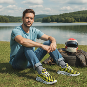 Man sitting on grass by a lake with checkered shoes and helmet.