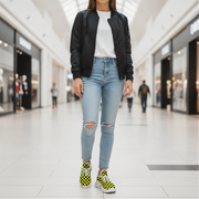Woman wearing a black jacket, white shirt, ripped jeans, and checkered shoes in a mall.