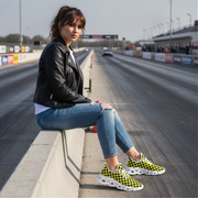 Woman sitting on a race track wearing black leather jacket, blue jeans, and checkered shoes.