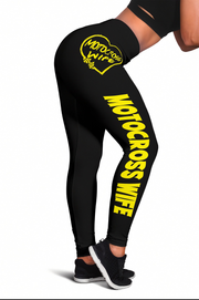 Black high-waisted leggings with bold yellow 'MOTOCROSS WIFE' text down the left leg and a yellow heart logo on the right hip, shown on a cropped model from the side against a white background.