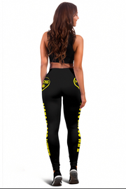 A woman shown from the back wearing black athletic leggings with bright yellow graphic text down the legs and a matching black sports bra, against a plain white background.