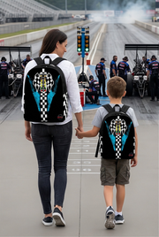 A young boy wearing a Carolina Blue drag racing backpack over his shoulders, standing in the pit area of a drag strip looking at a light blue dragster being prepped by a mechanic on a sunny afternoon.