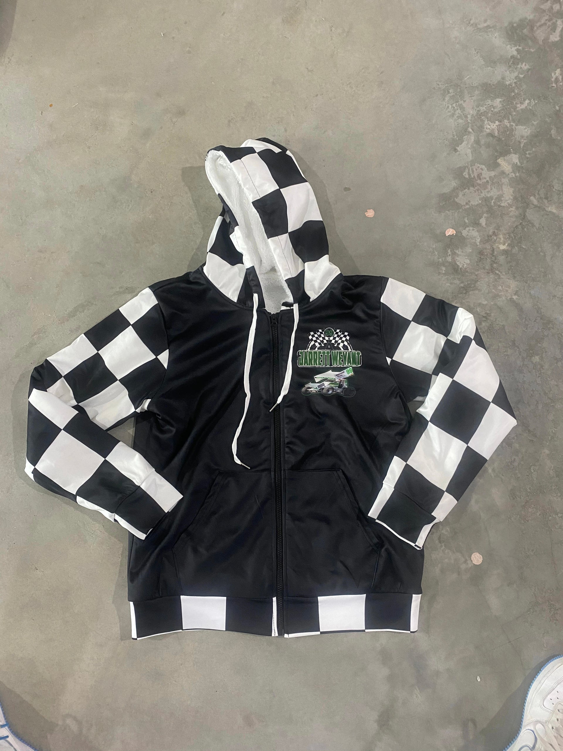 A personalized racing jacket displayed on a mannequin, featuring a large, high-resolution photo of a custom muscle car printed on the back panel, complemented by black and white checkered flag accents on the sleeves and a plush, cream-colored sherpa lining visible at the collar.
