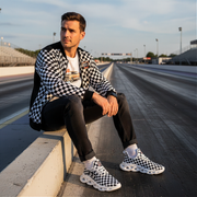 man sitting at a dragstrip wearing a checkered jacket with a custom checkered shoes