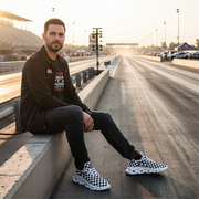 man sitting at a drag racing track wearing a back jacket with a custom checkered shoes number 33