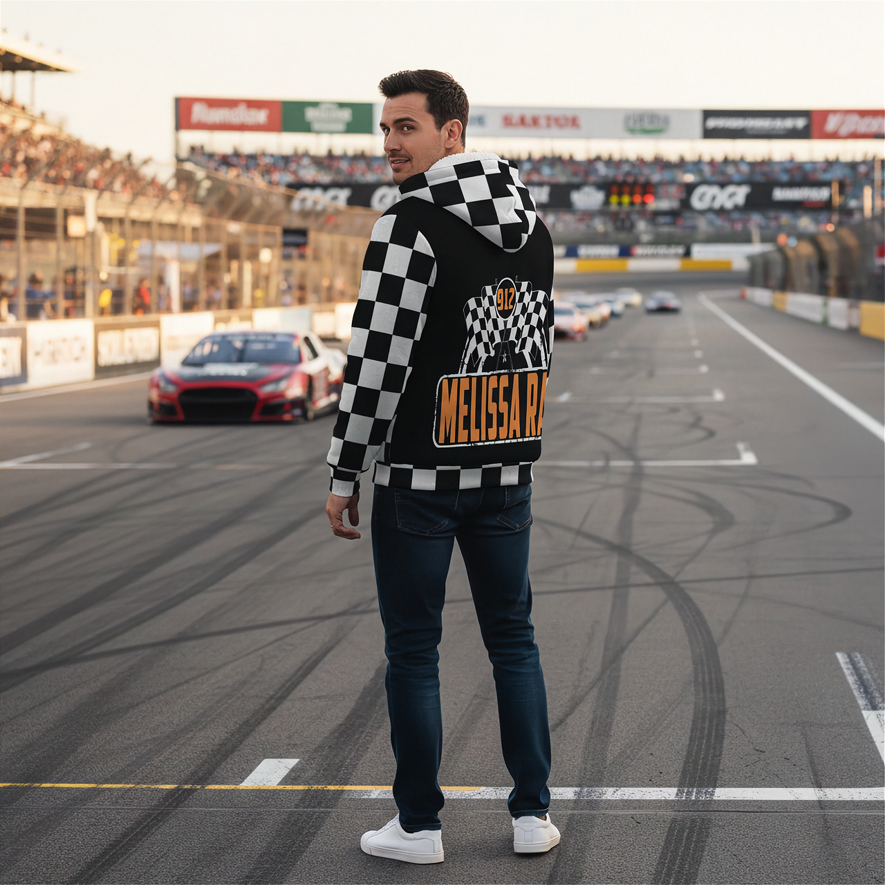 A race fan wearing a custom-printed sherpa-lined racing jacket while standing in the grandstands of an illuminated dirt track at night, with the race cars visible in the background.