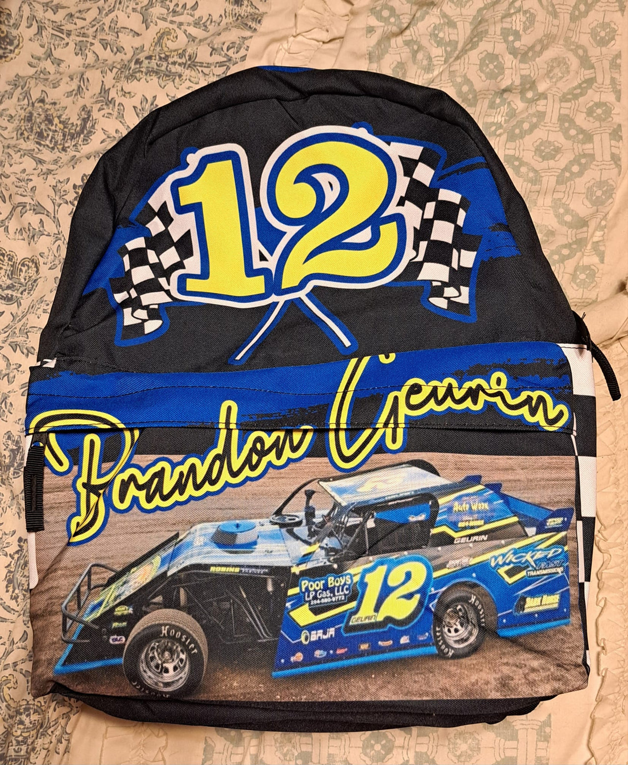 A checkered backpack with a racing theme, featuring a large main compartment and a front utility pocket. The backpack is custom-made with a blue and black checkered pattern and has a graphic of a racing car with the number 12 and the name 'Brandon Geurin'.