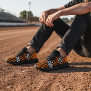 man wearing orange and black patterned sneakers sitting on a dirt surface.