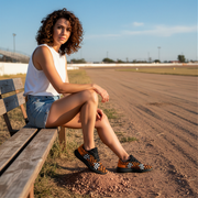 Woman sitting on a wooden bench by a race track wearing a dirt checkered shoes