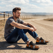 Man sitting on a dirt road wearing orange and black patterned shoes.