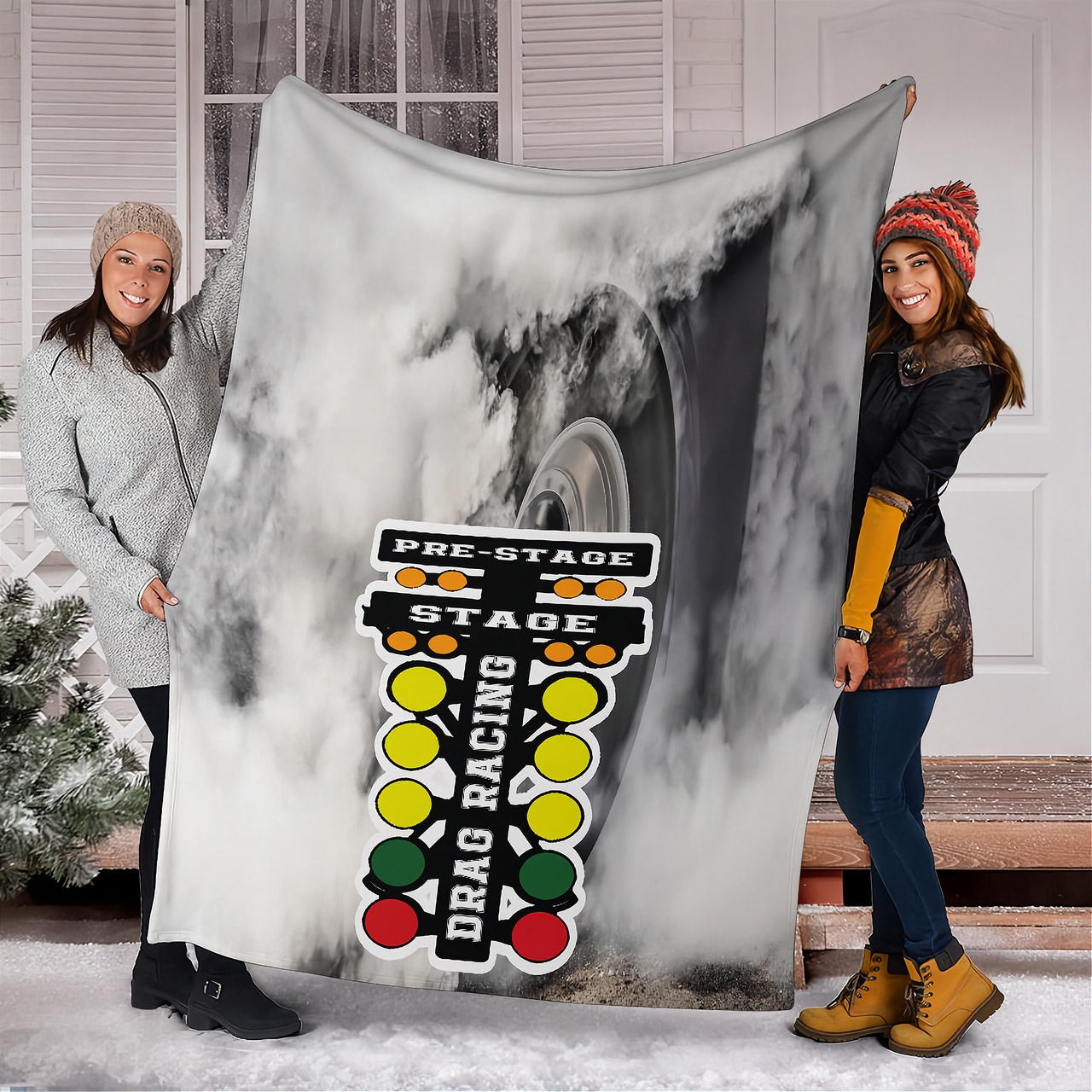 Two woman holding a large blanket with drag racing design outdoors.