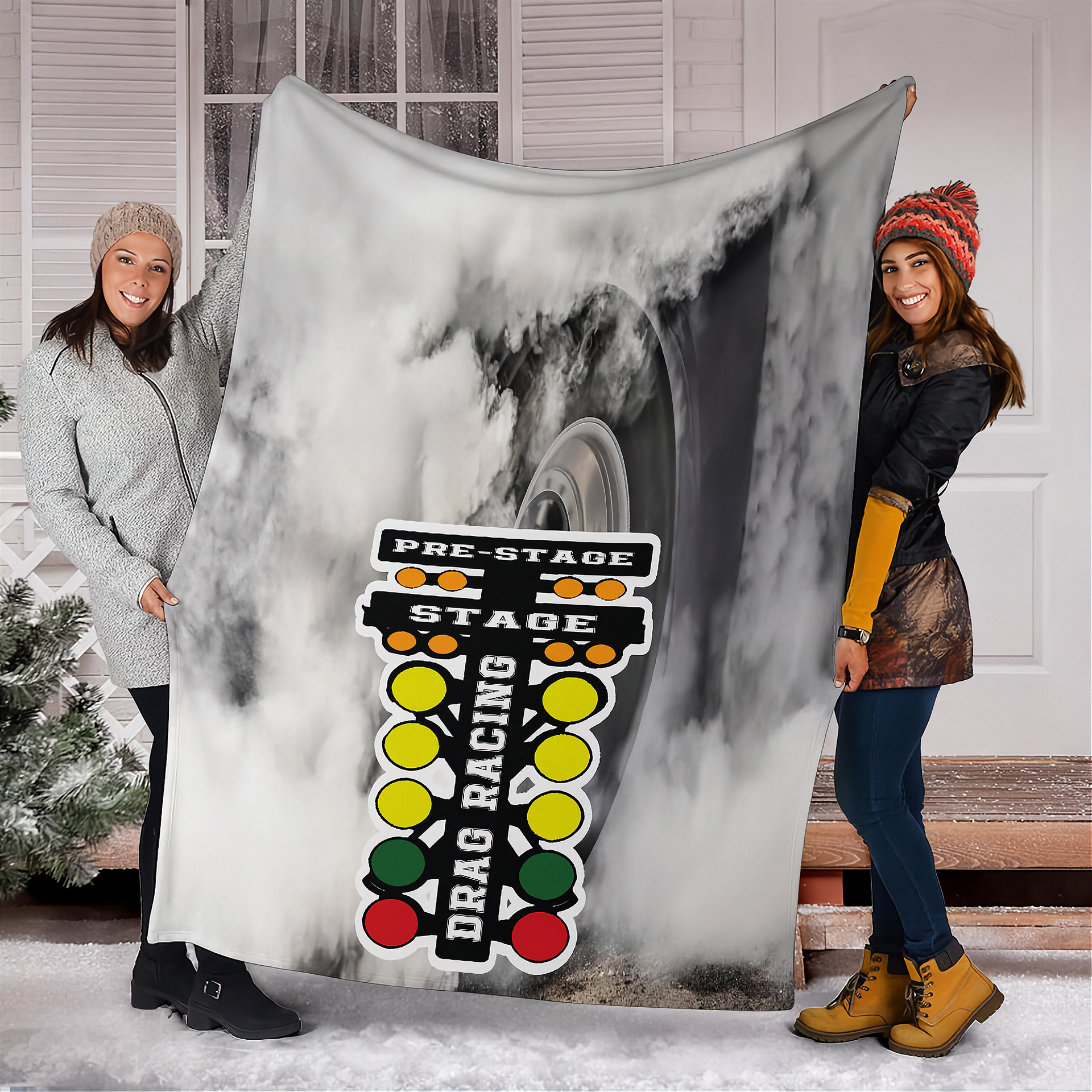Two woman holding a large blanket with drag racing design outdoors.