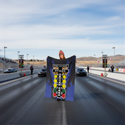 woman holding a 'Stage 2 Drag Racing' blanket at a race track.