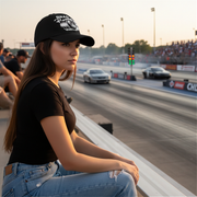 Woman sitting at a drag race track with cars  on the side wearing a drag racing baseball cap