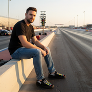 Man sitting on a race track with cars in the background wearing a drag racing tree logo sleep ons shoes